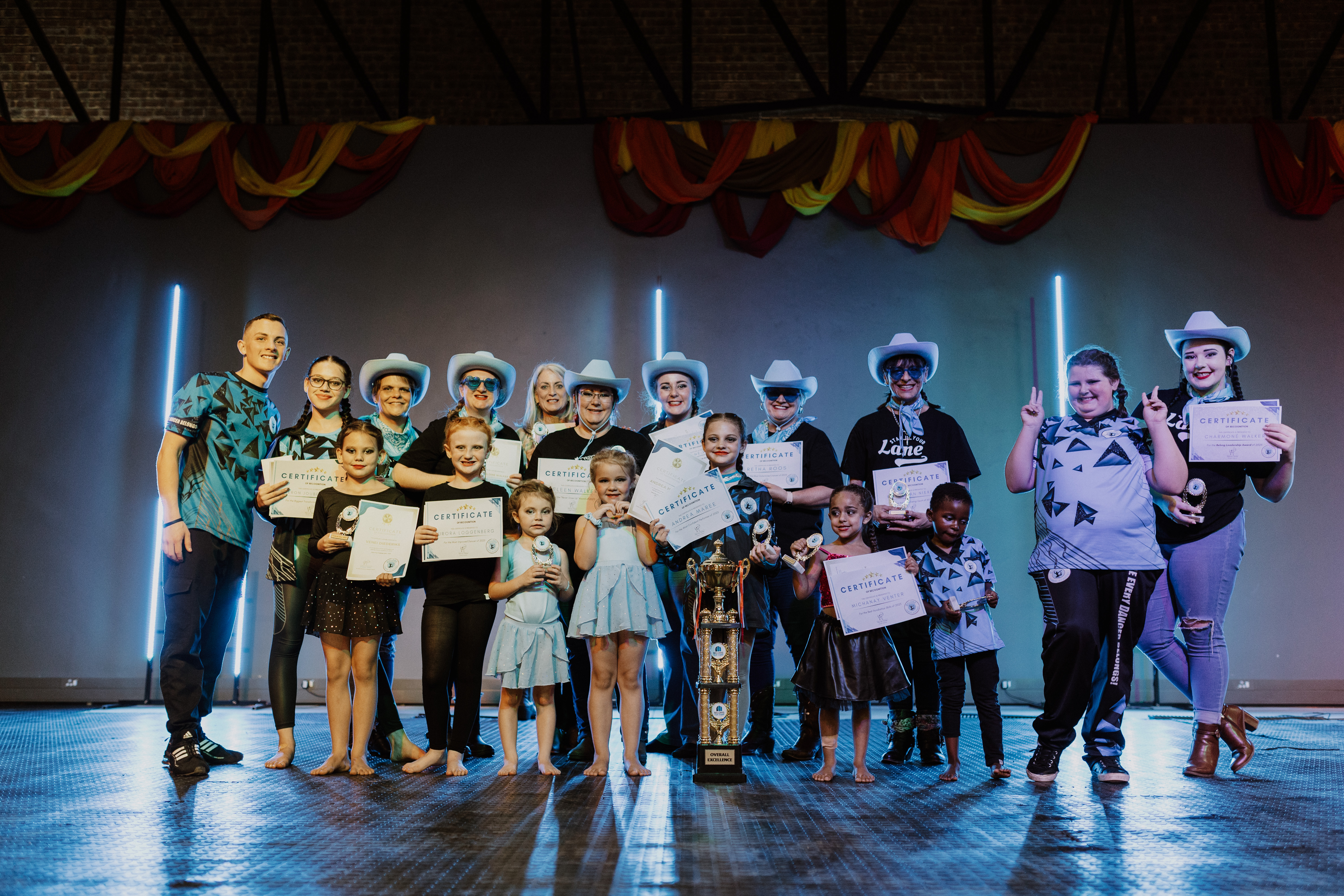 Belong students and coaches posing on stage with certificates and trophies